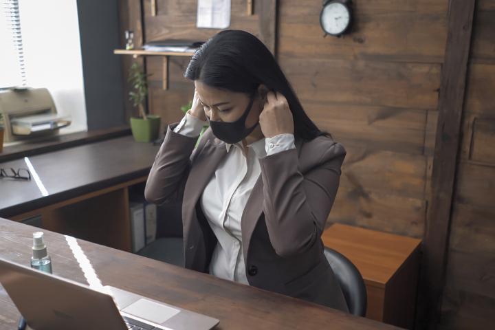 Woman sitting at a desk and adjusting her face mask.