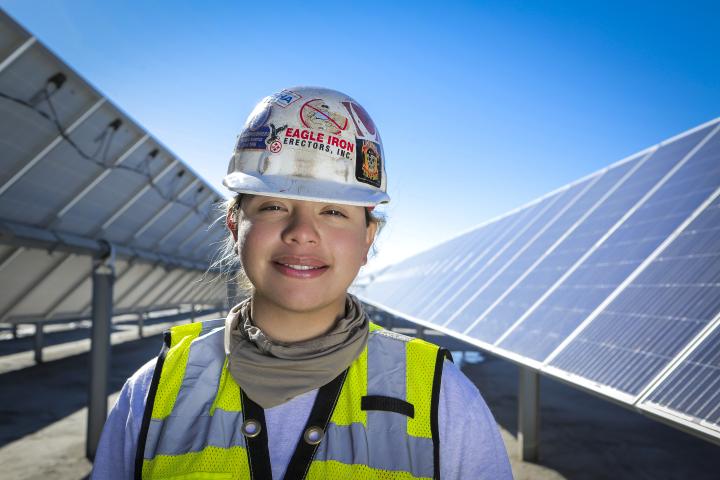 Union woman worker wearing a hard hat and standing in front of solar panels