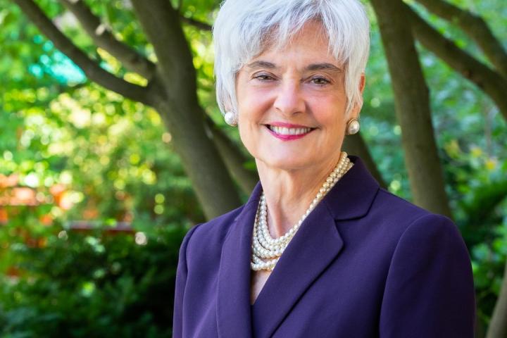 Susanne Bruyère, wearing a purple blazer with several strands of white pearls and matching earrings